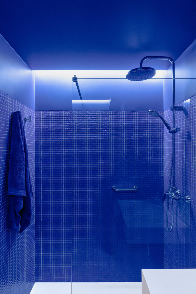 A modern shower with blue tiles, a rain showerhead, and a towel hanging on a hook.