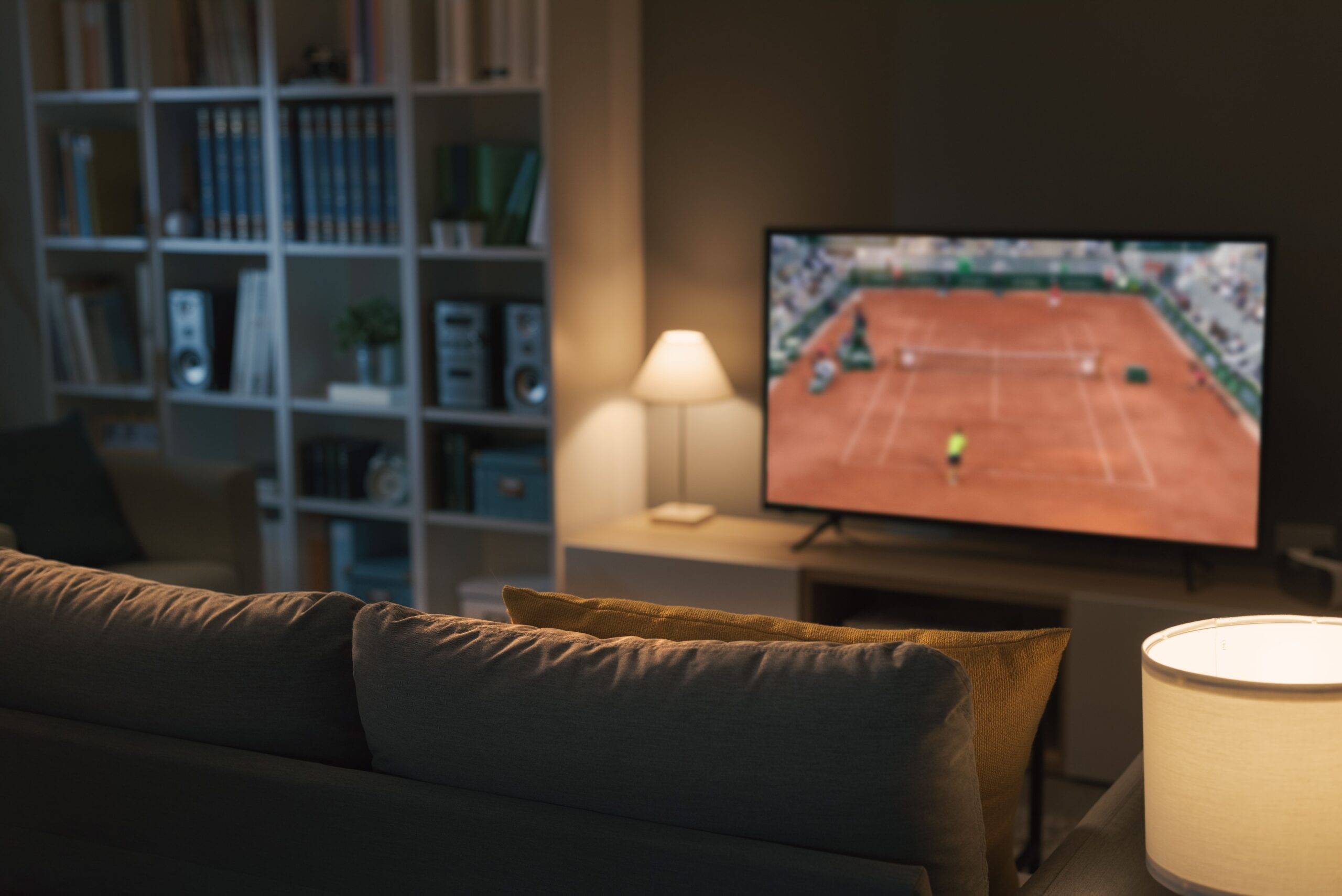 A couch facing a TV that's playing a tennis game.