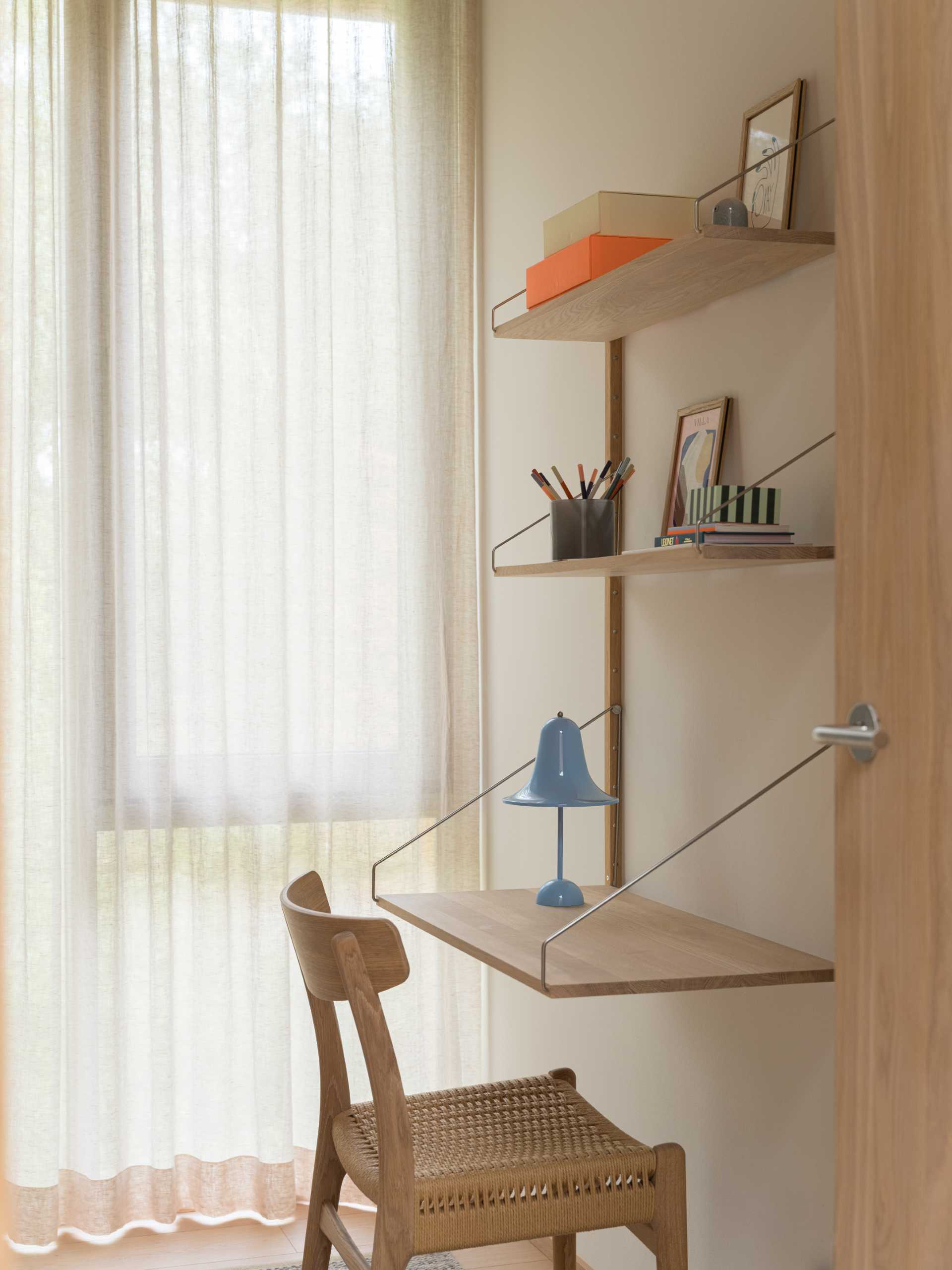 A modern bedroom with a wall-mounted desk that also includes shelving above.