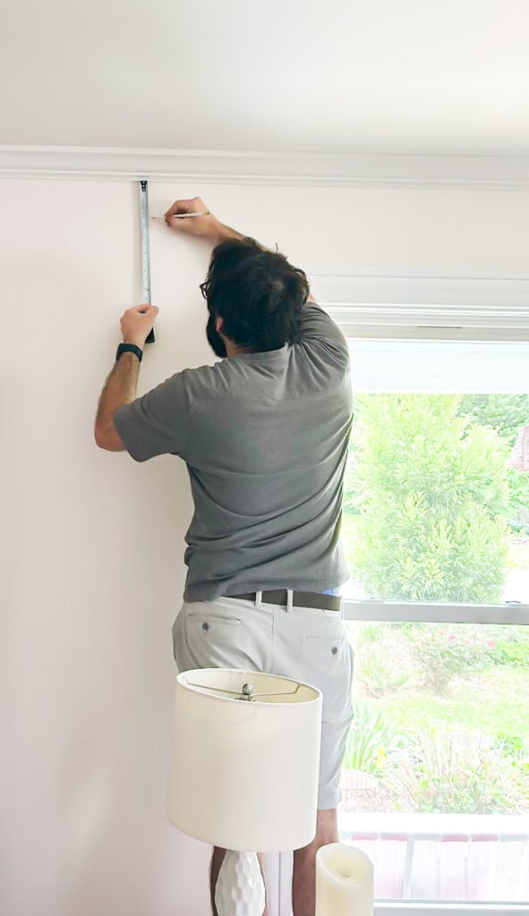measuring wall around window to figure out where to hang curtain rod.