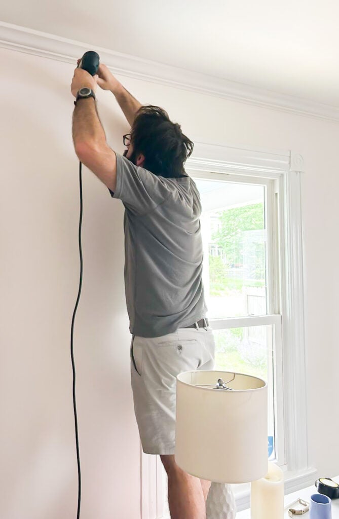 man drilling holes in wall to hang a curtain/drapery rod.