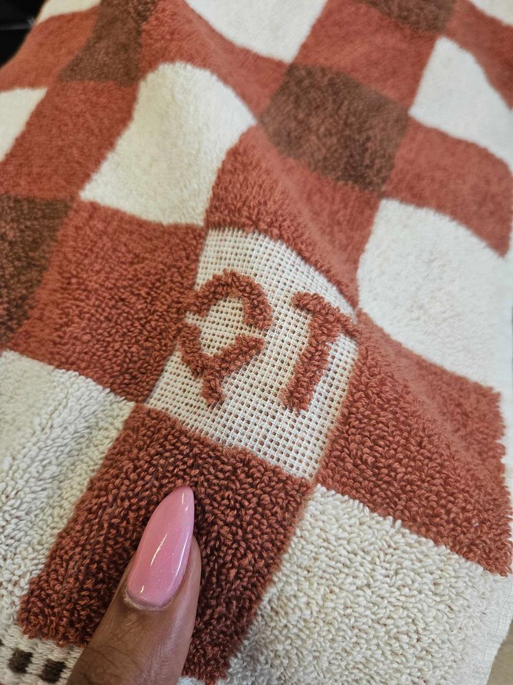 Person's hand holding a bath towel with brown checkered design to show it's texture.
