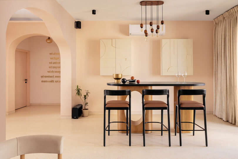 Modern dining area with a black table, four chairs, minimalist wall art, warm neutral tones, and an arched doorway leading to another room.